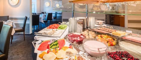 Zona de bufé con diversas opciones de comida, incluyendo frutas, postres y bebidas.