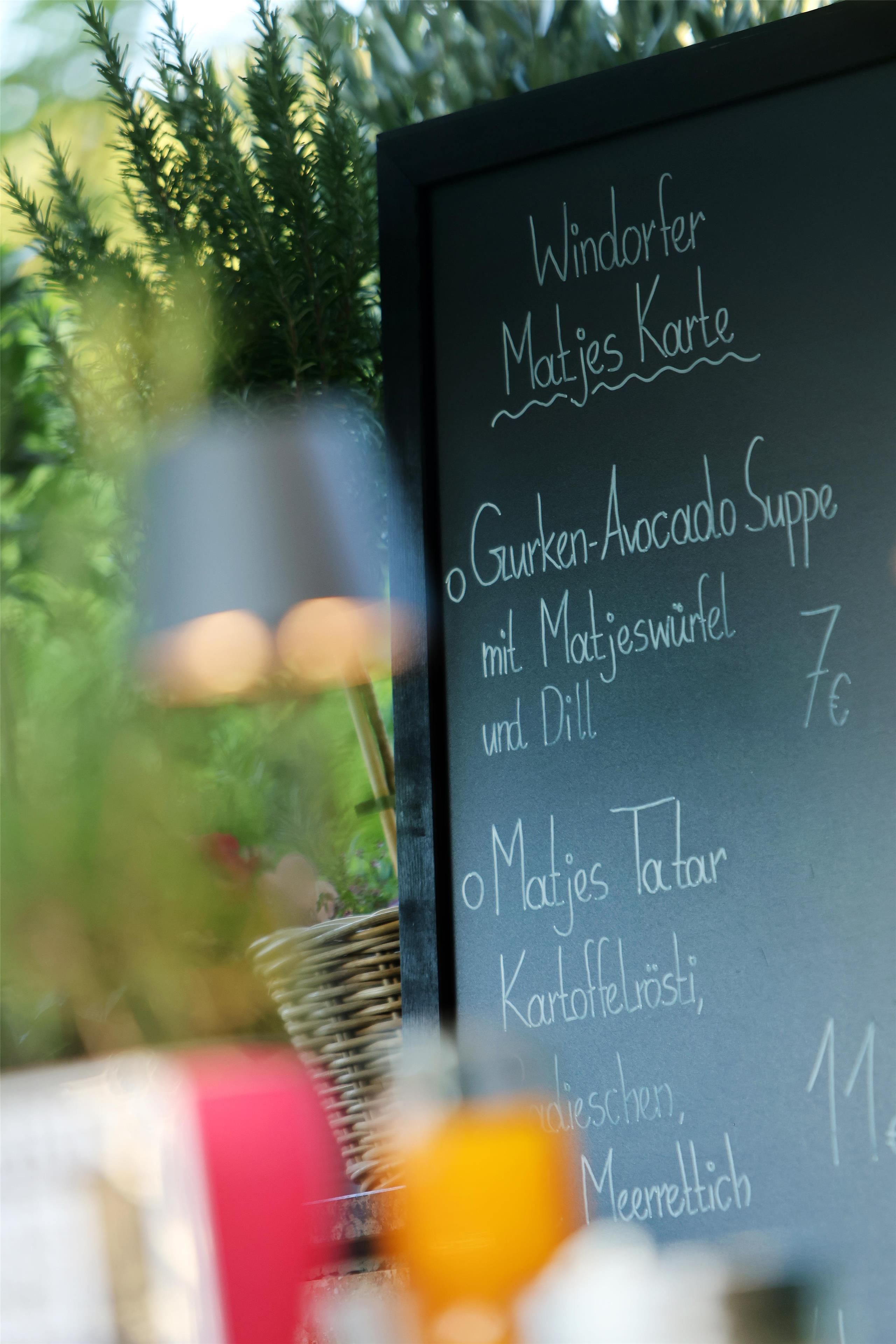 Een schoolbordmenu met gerechten zoals 'Gurken-Avocado Soep' en 'Matjes Tatar'.