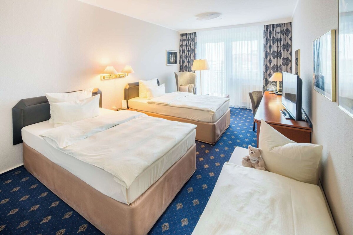 A hotel room with two beds, a desk, a chair, a television, and a teddy bear.
