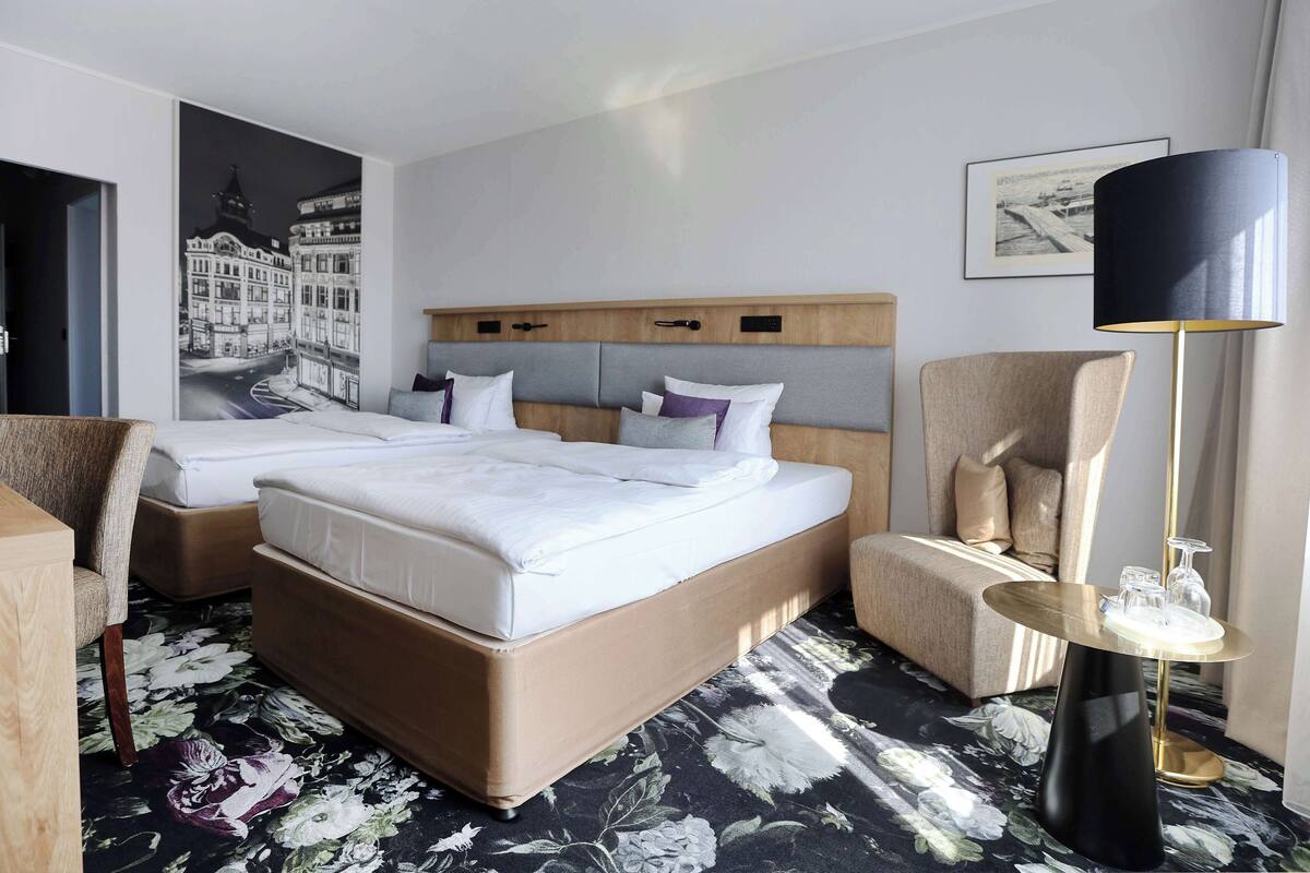 A hotel room with a large bed, two bedside tables, a chair, a floor lamp, and a floral carpet.
