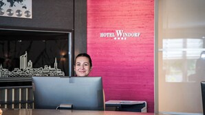 A reception desk with a cityscape model, a red wall with 'HOTEL WINDFORD' signage, and a window with natural light. - Best Western Hotel Windorf (Leipzig)