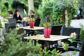 Un espacio al aire libre con mesas y sillas, algunas con plantas en macetas.
