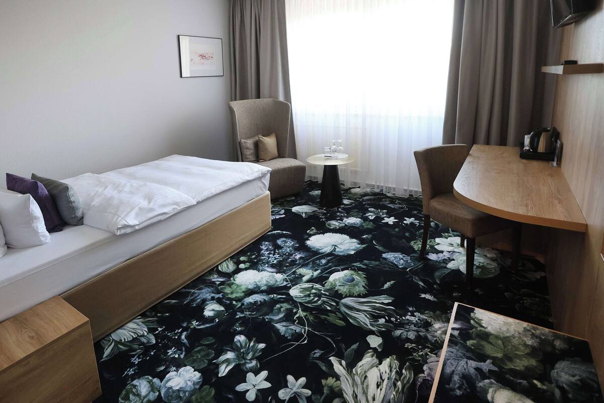 A hotel room with a bed, a sofa, a small table, a chair, and a TV.