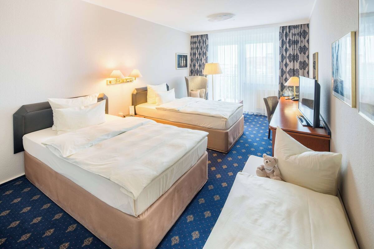 A hotel room with two beds, a desk, a chair, and a television.