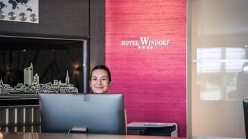 Ein Empfangsschalter mit Stadtmodell, eine rote Wand mit der Beschilderung 'HOTEL WINDORF' und ein Fenster mit Tageslicht.