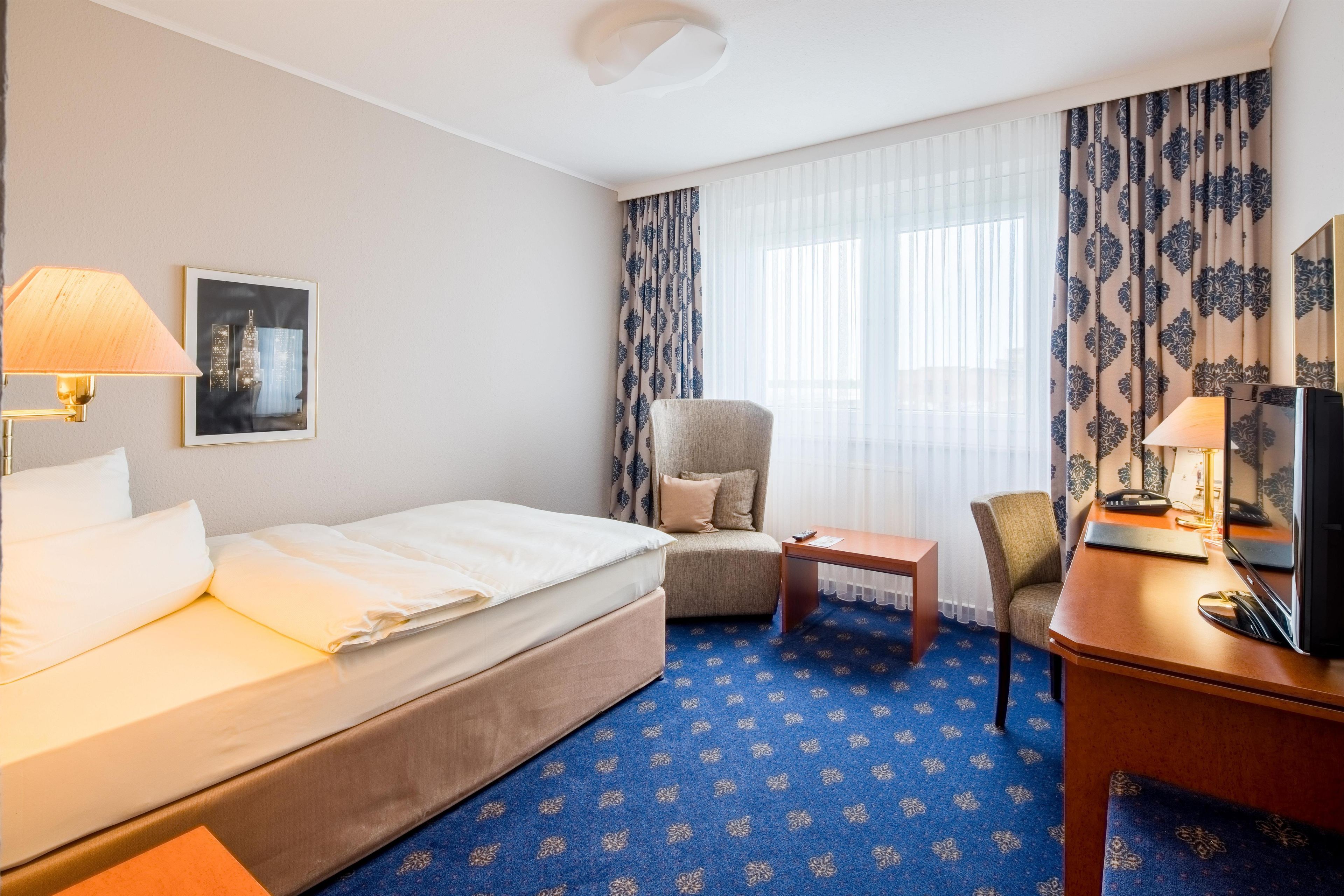 Ein Hotelzimmer mit Bett, Stuhl, Schreibtisch, Lampe und Fernseher.