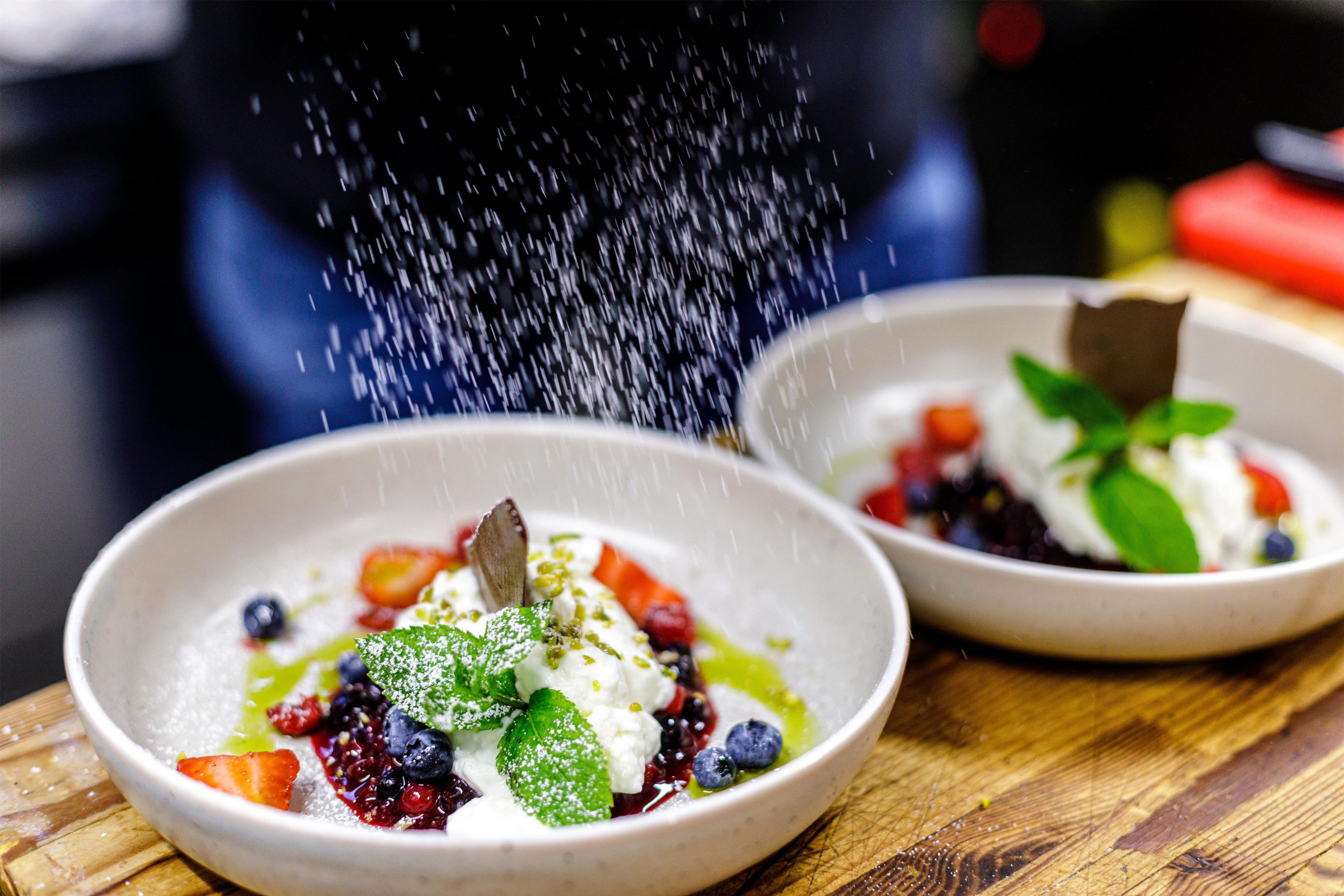 Dos tazones de postre con frutos rojos y hojas de menta, espolvoreados con azúcar glas, sobre una superficie de madera.