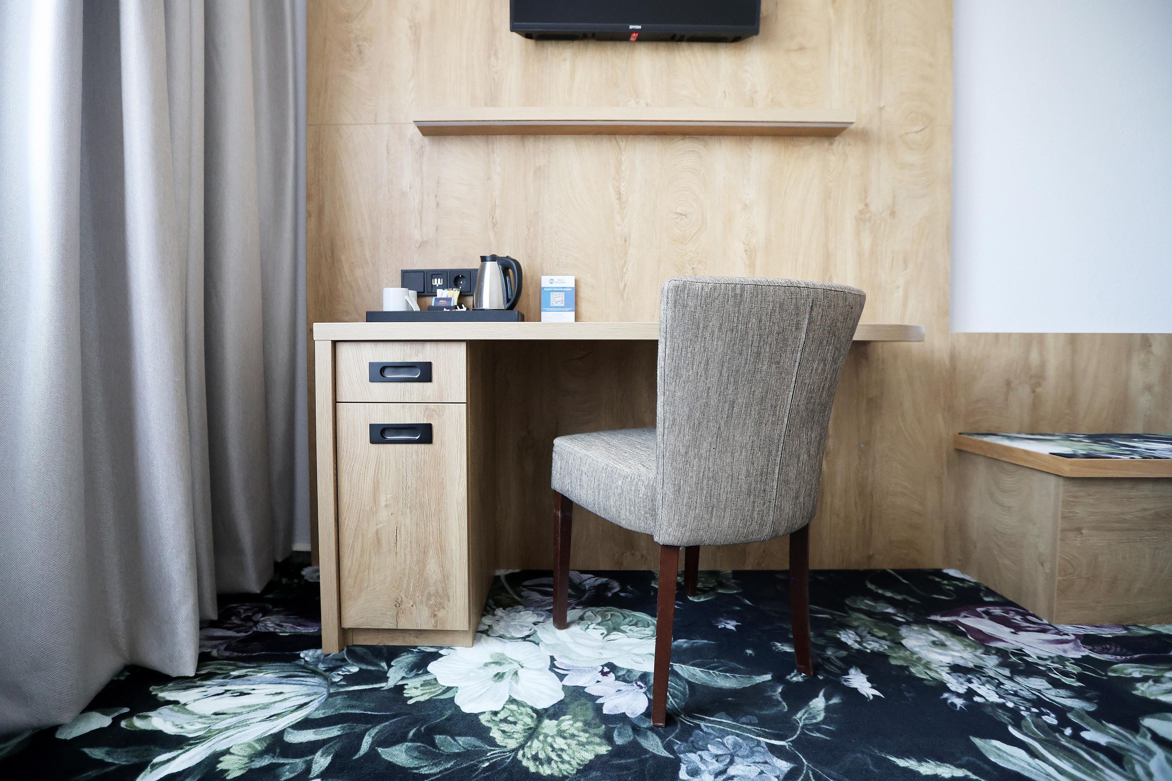 Ein Hotelzimmer mit einem Holztisch, einem Sessel, einem wandmontierten Flachbildfernseher und einem Teppich mit Blumenmuster.
