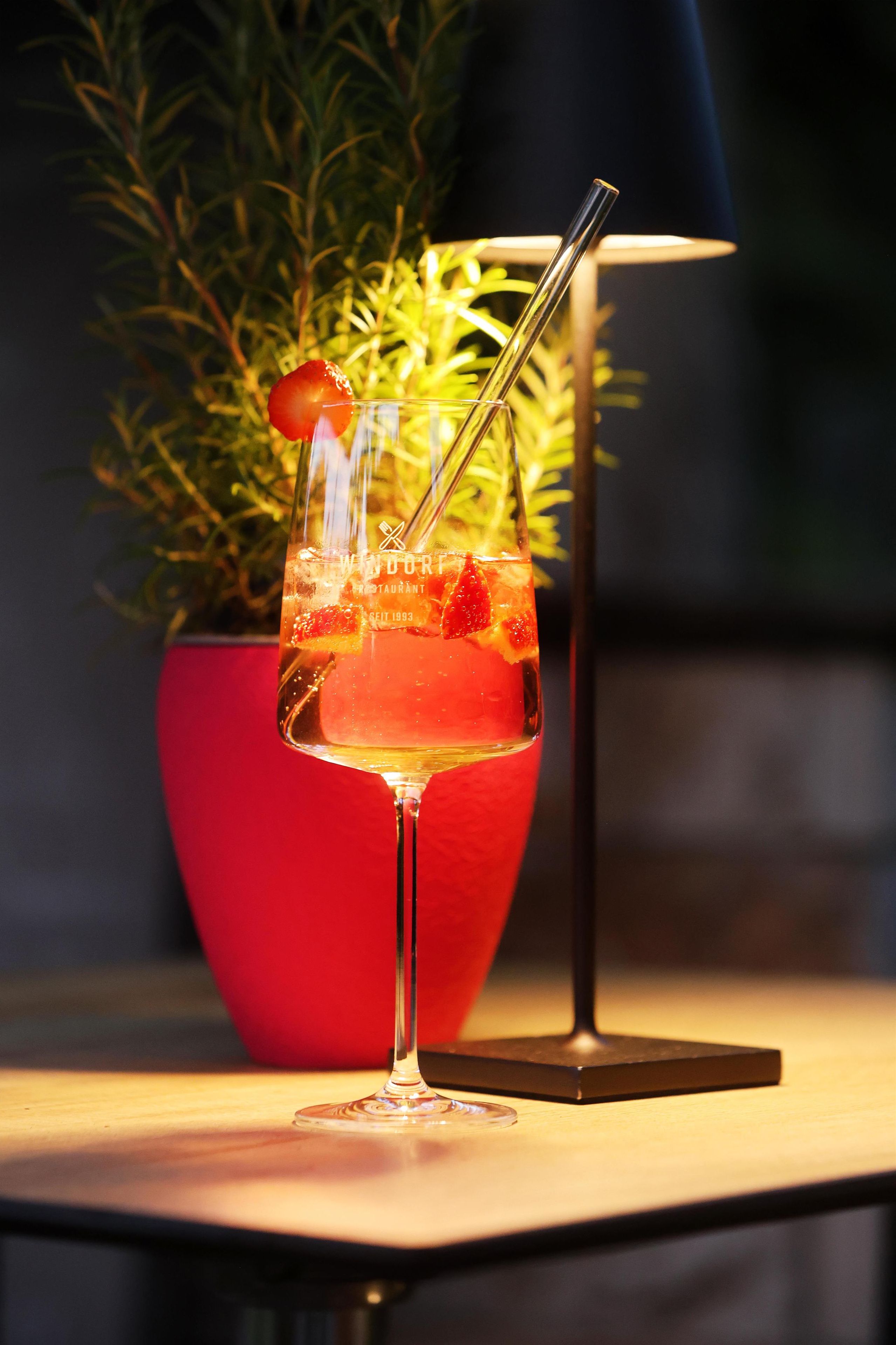 Un verre à cocktail avec une paille et une fraise en guise de décoration, posé sur une table en bois.