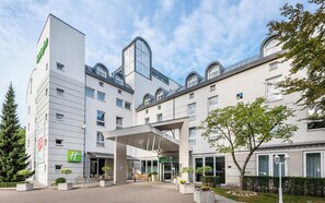 A modern hotel with a covered entrance, outdoor seating, and a landscaped garden. - Holiday Inn Luebeck by IHG (Lübeck)