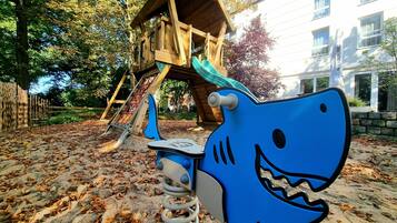 Un parque infantil con un columpio con forma de tiburón azul y una estructura de madera para escalar.