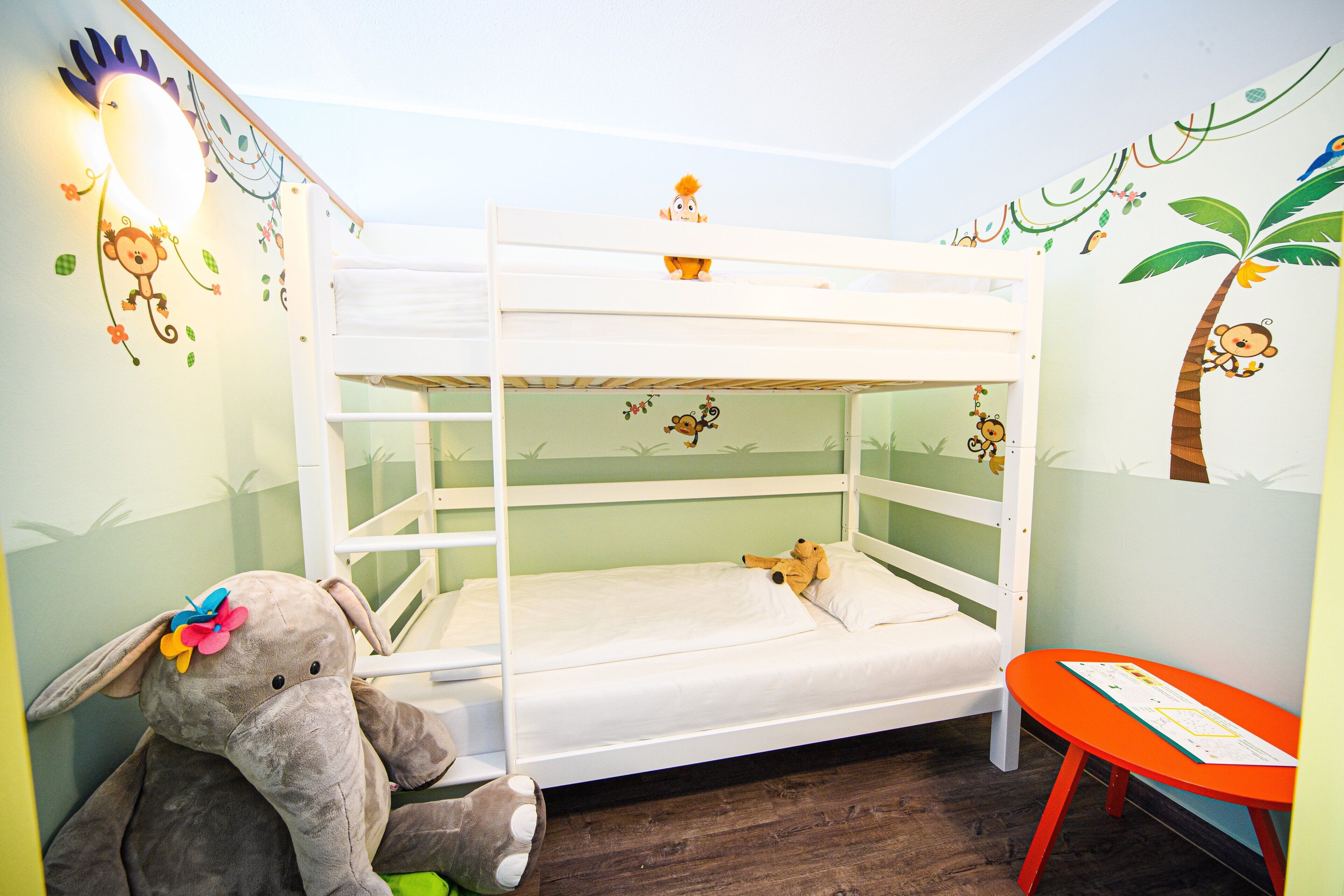 A bunk bed with a white frame, a small table, and a wall with animal and plant decorations.