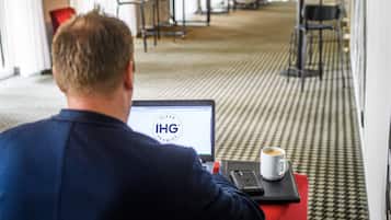 Un homme est assis à un bureau, devant un ordinateur portable dont l’écran affiche le logo « IHG », et il a une tasse de café à portée de main.
