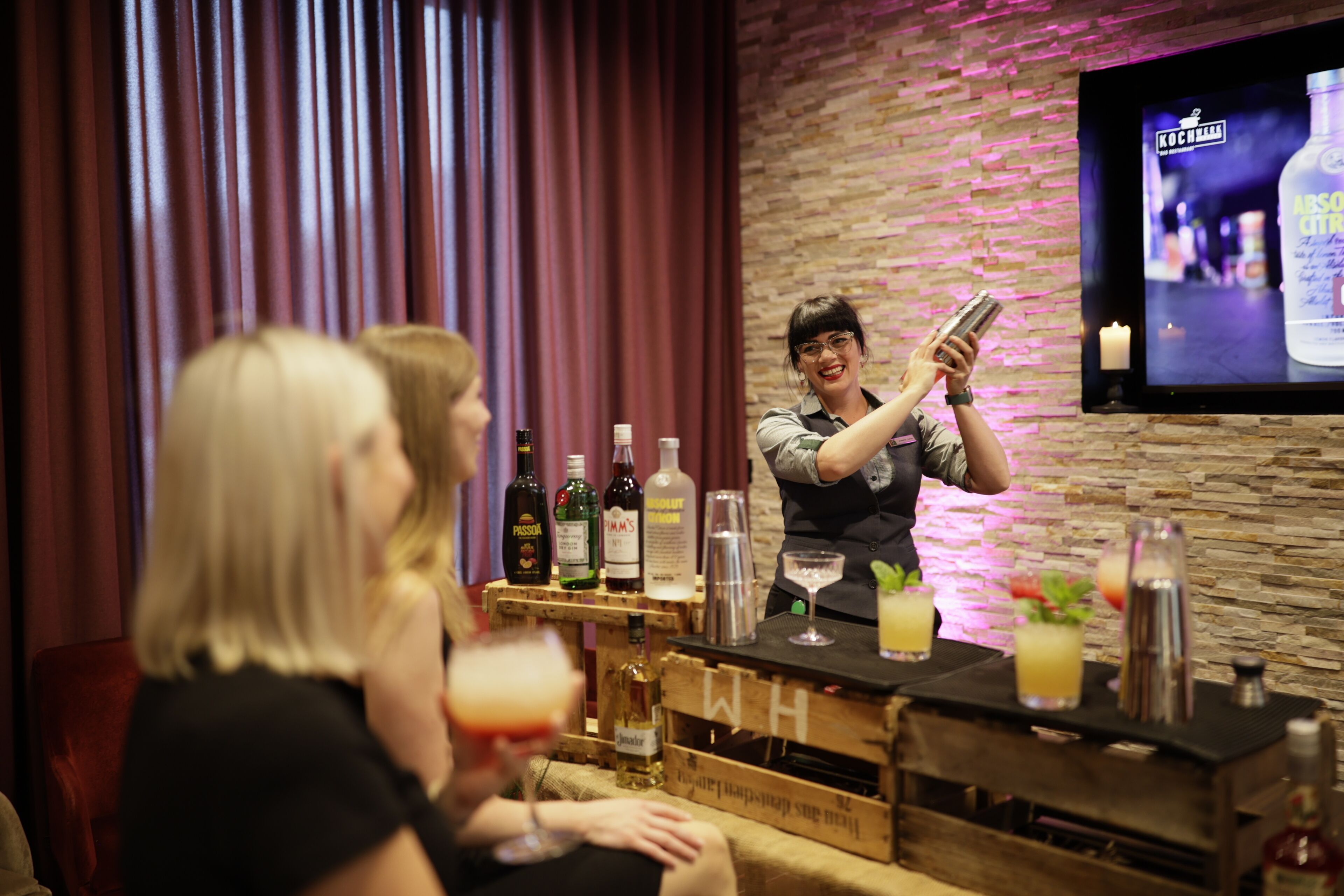 A bar area with a bartender preparing drinks, bottles of alcohol, and glasses on a wooden bar counter.