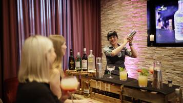 A bar area with a bartender preparing drinks, bottles of alcohol, and glasses on a wooden bar counter.