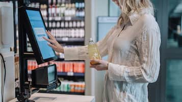 Eine Person bedient sich an einem Automaten in einem Geschäft, im Hintergrund Regale mit Produkten.