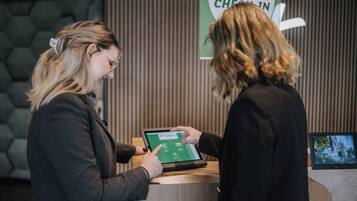 Two individuals interacting with a tablet at a reception desk in a hotel lobby.