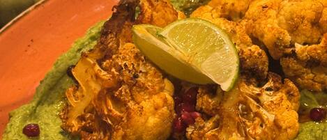 A plate of food with grilled chicken, avocado, and lime on an orange plate.