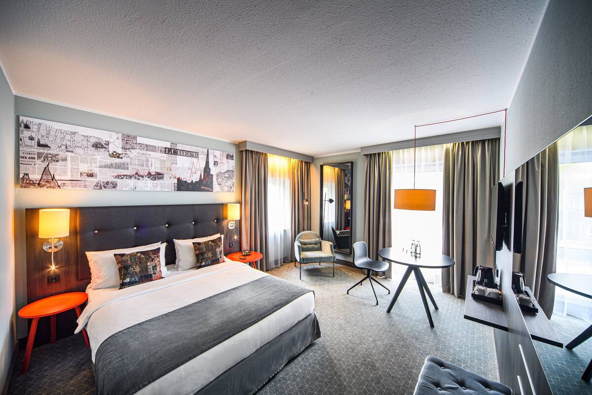 Quarto de hotel com uma cama grande, uma escrivaninha, uma cadeira e uma televisão.