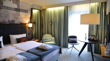 A hotel room with two beds, a desk, a chair, a lamp, and a large window with curtains.