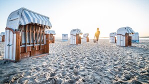 Beach huts with striped awnings and wooden doors, arranged in a row on a sandy beach. - Holiday Inn Luebeck by IHG (Lübeck)