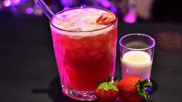 A cocktail glass with a strawberry garnish, a glass of milk, and two strawberries on a table.