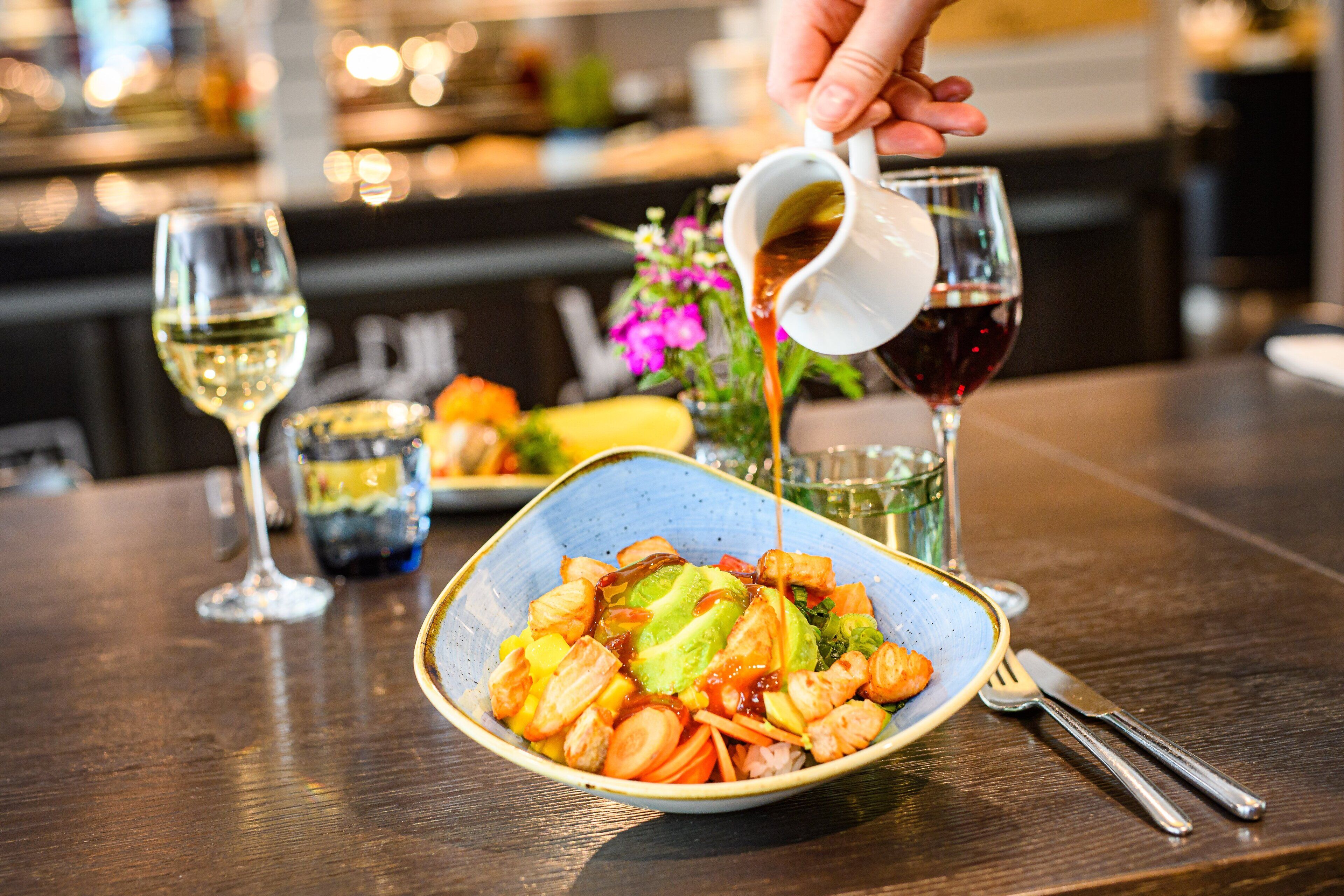 A dining table with a bowl of food, a glass of white wine, and a glass of red wine.