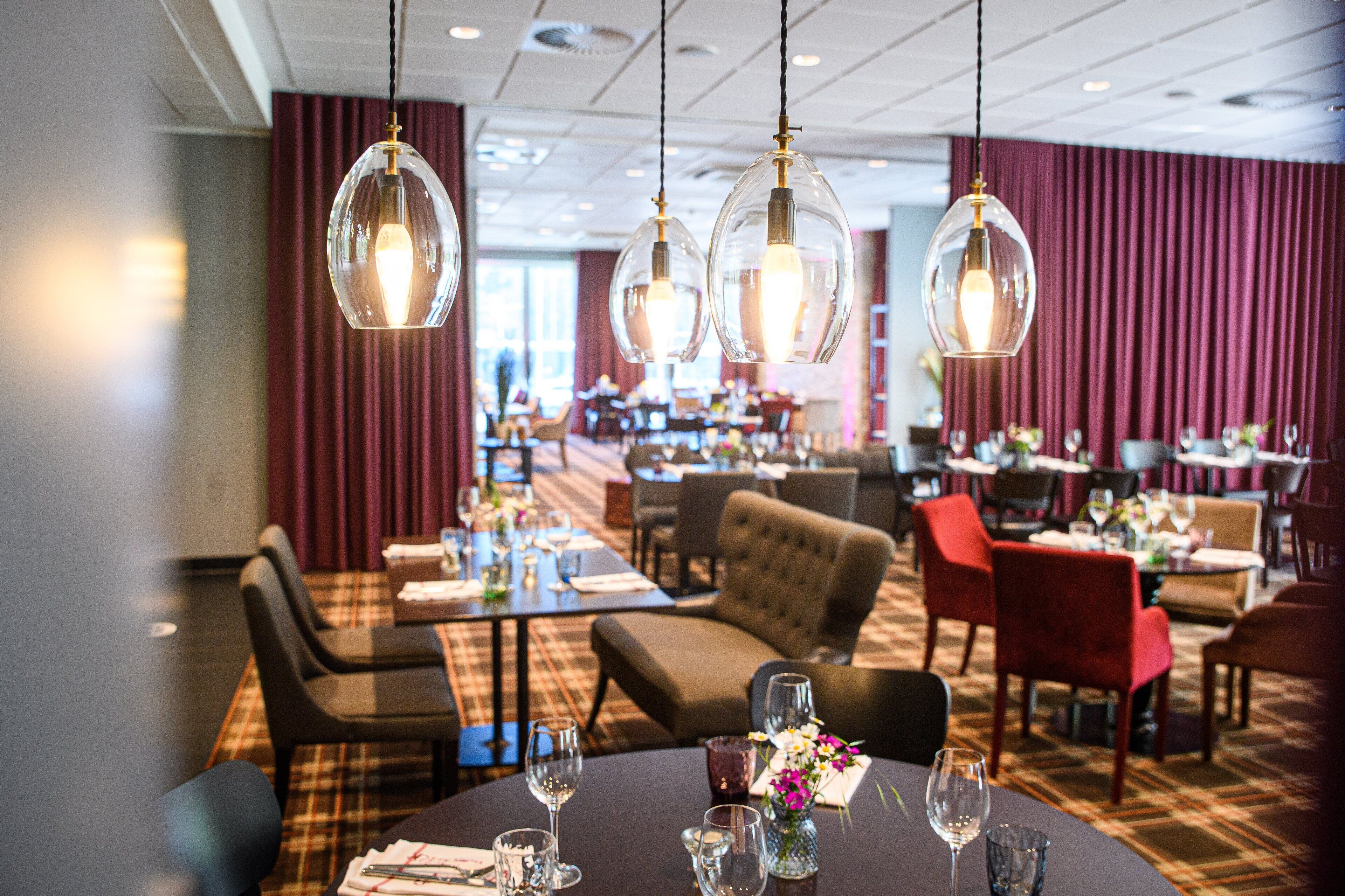 A restaurant with round tables, red chairs, and hanging glass lamps.