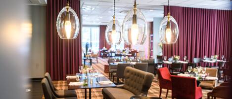 A restaurant with round tables, red chairs, and hanging glass lamps.