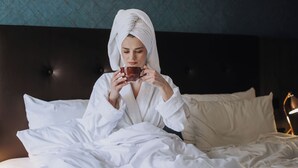 A person in a robe sitting on a bed with a tray of breakfast items. - Holiday Inn Luebeck by IHG (Lübeck)