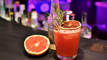 A glass of red beverage with a slice of citrus and a sprig of rosemary, accompanied by a half grapefruit and a bottle labeled "FEVER."