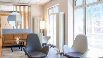 Ein modernes Interieur mit einem Sofa, zwei Sessel, einem runden Tisch und einem großen Fenster.