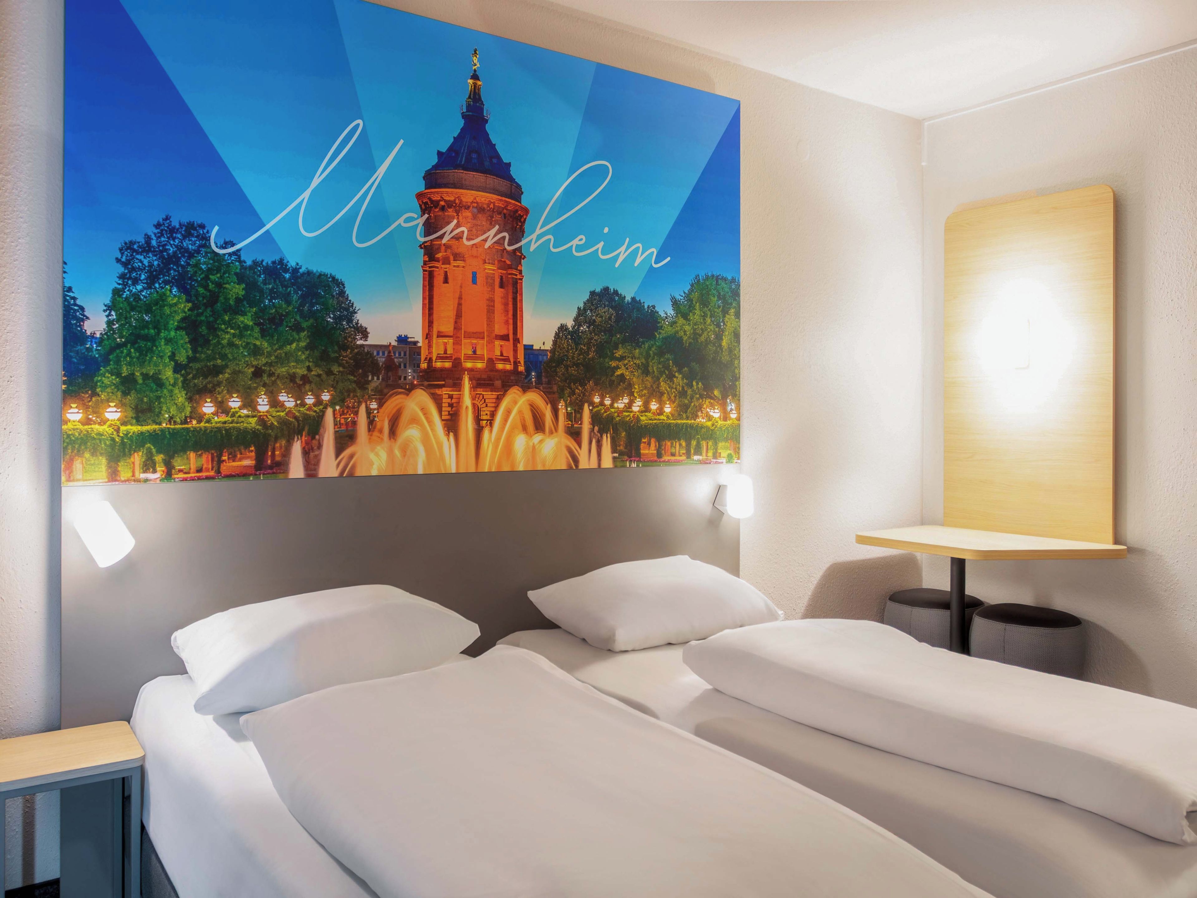 Habitación de hotel con cama, mesita de noche, lámpara de pared y un cuadro con una torre.