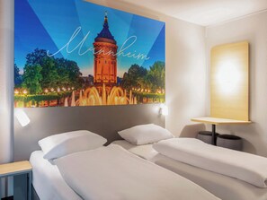 Habitación de hotel con cama, mesita de noche, lámpara de pared y un cuadro con una torre.