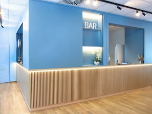 Una recepción con un cartel de 'BAR', una planta en maceta y una computadora portátil sobre el mostrador.