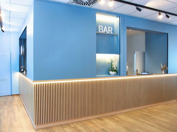 A reception desk with a 'BAR' sign, a potted plant, and a laptop on the counter.