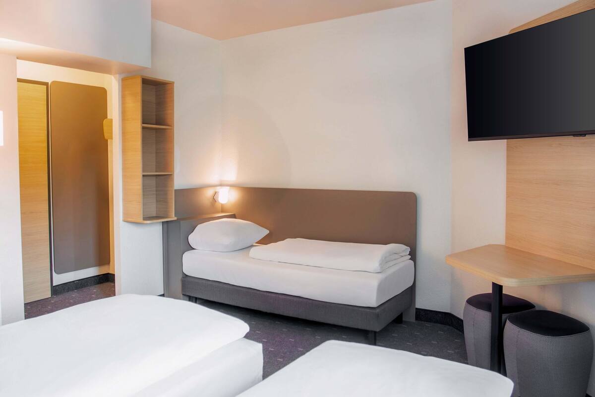 A hotel room with a bed, a TV, a wardrobe, and a small table.