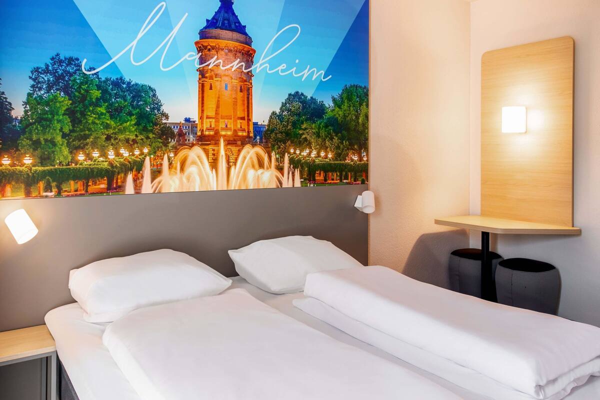 A hotel room with two beds, a wall-mounted lamp, and a poster of a tower.