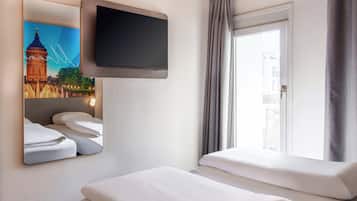 Une chambre d’hôtel dotée d’un téléviseur à écran plat fixé au mur, d’un lit avec une literie blanche, d’une fenêtre avec des rideaux et d’un tableau représentant un pont.