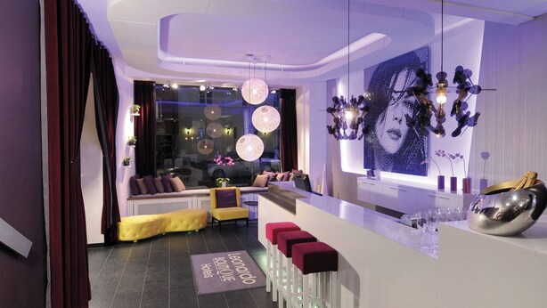 Un hall d’hôtel moderne doté d’un bar, de coins salon et d’une grande œuvre d’art accrochée au mur.