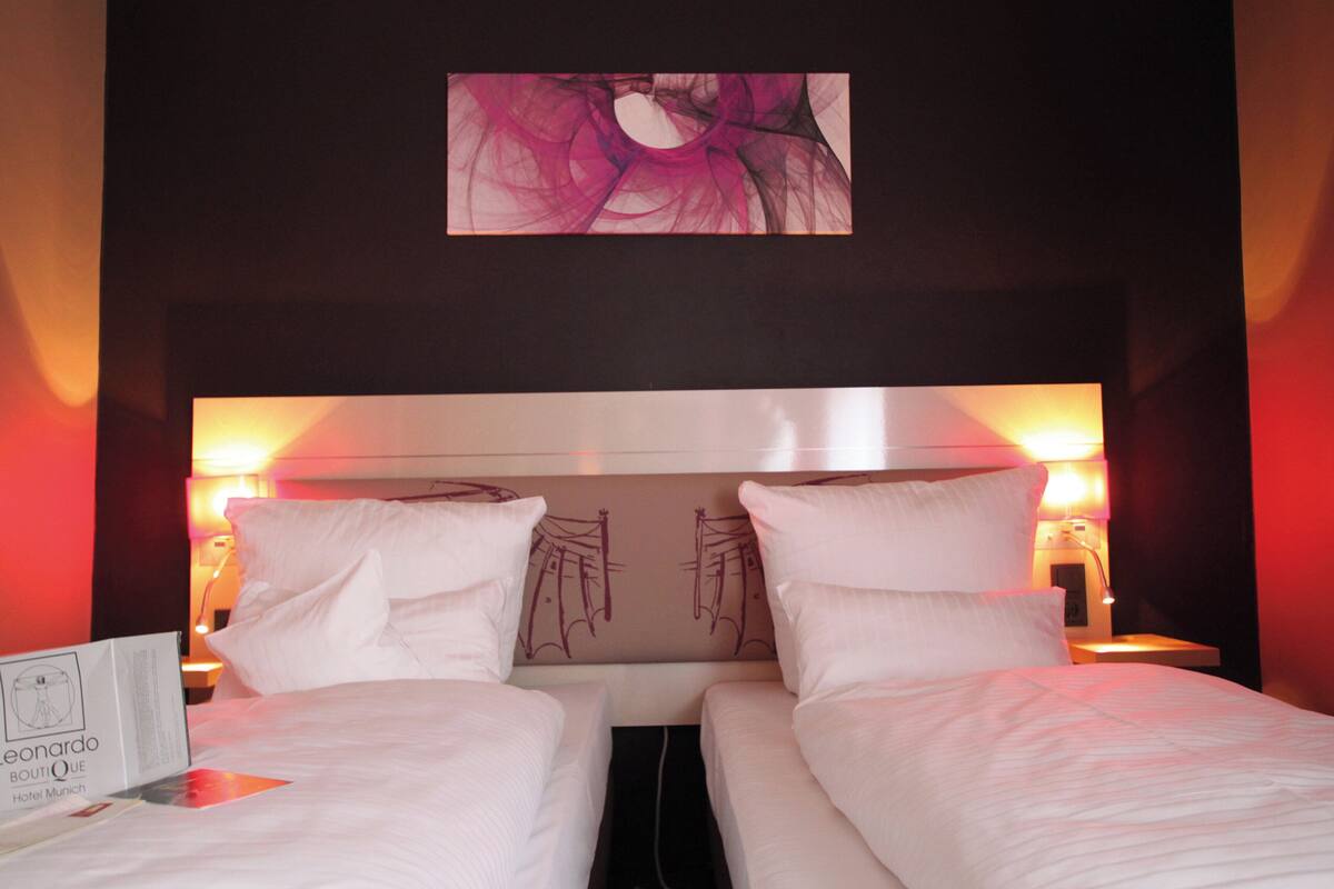 Een hotelkamer met twee bedden, een hoofdeinde met een bloemistisch kunstwerk en bedlampen.