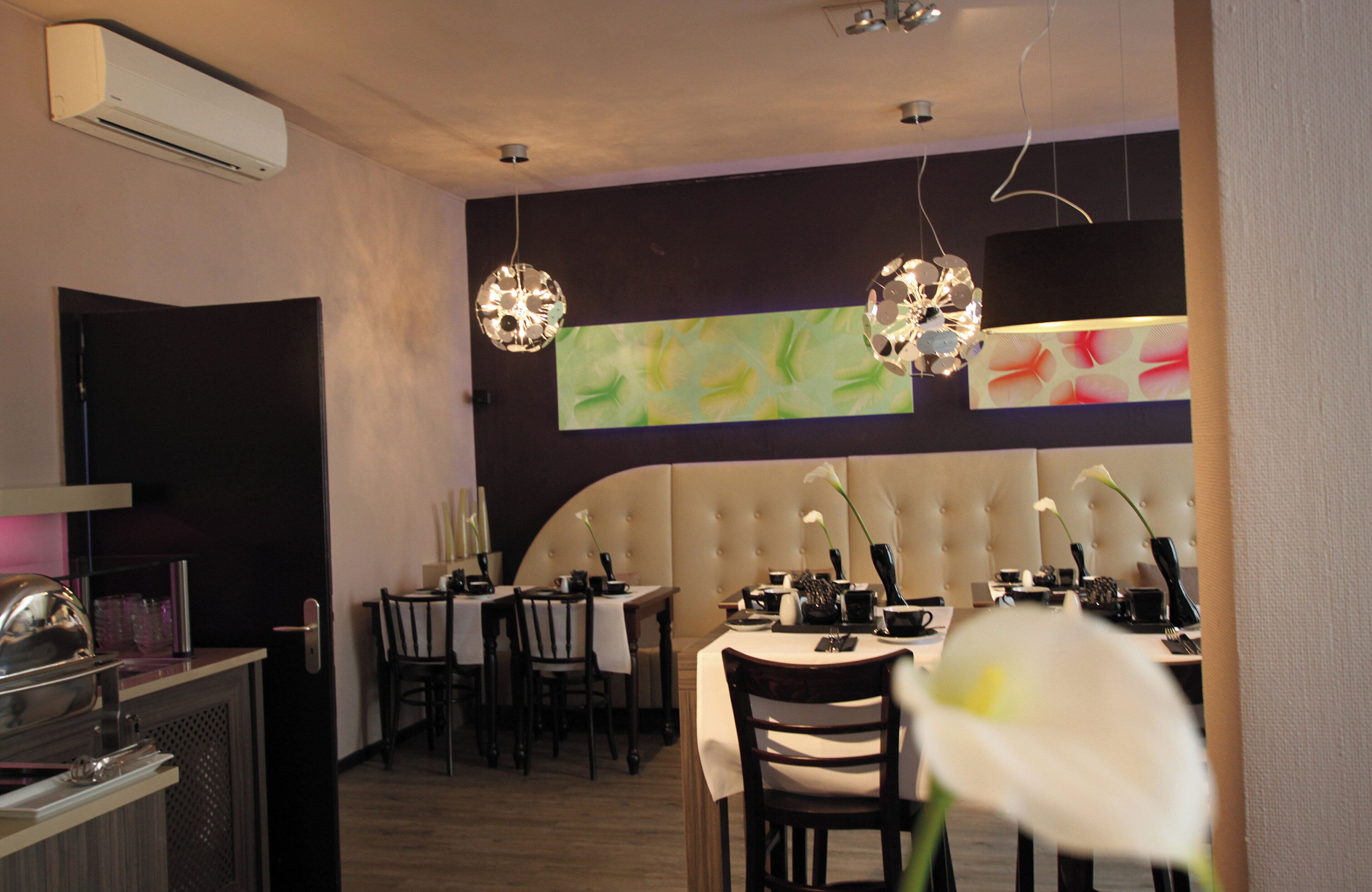 A restaurant with a modern interior, featuring a dining area with round tables and chairs, a bar area, and a large wall with abstract art.