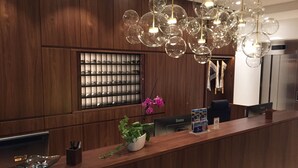 A reception desk with a wooden panel backdrop, a glass display case, and a modern chandelier. - Hotel Antares (Munich)