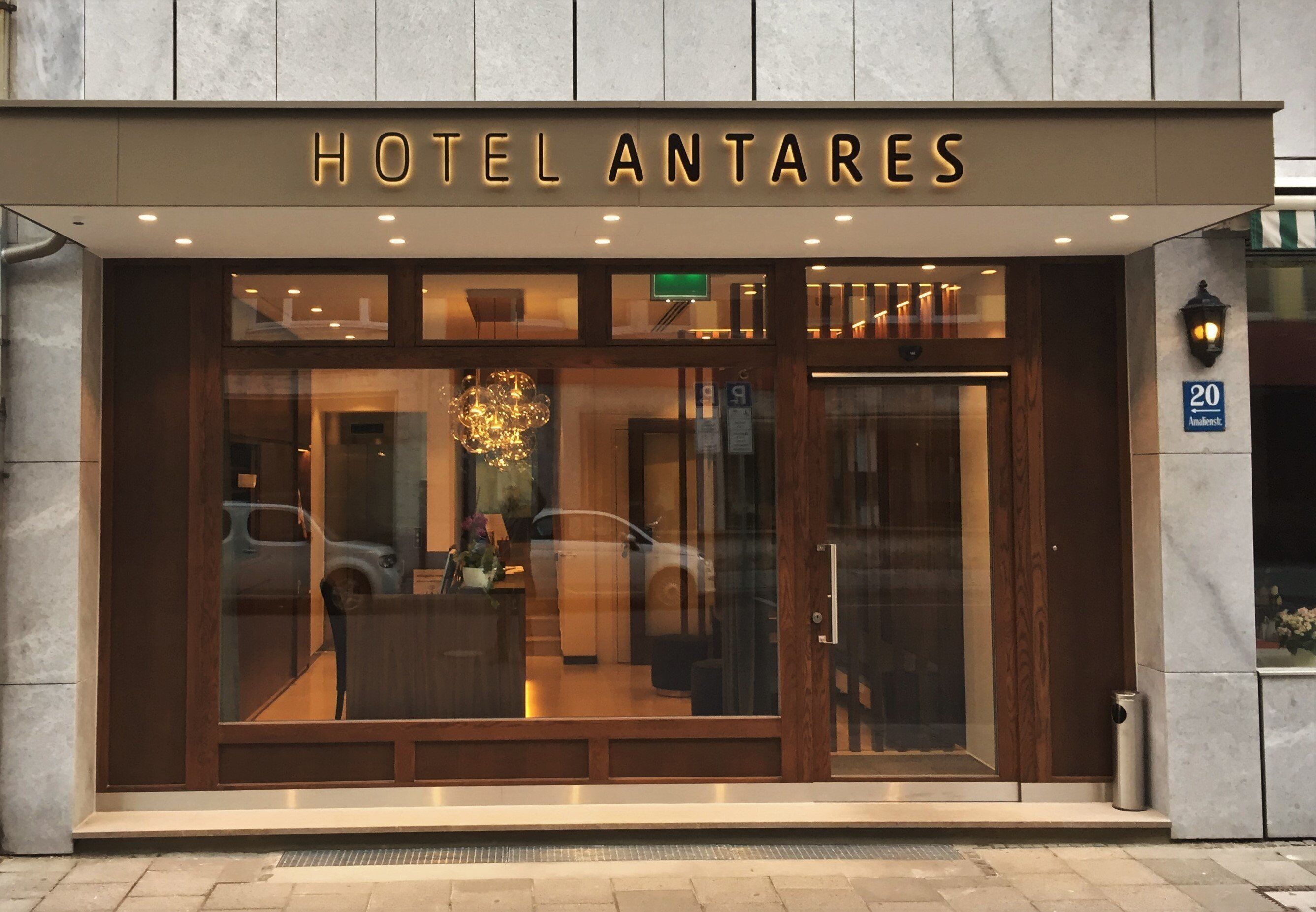 Das Hotel Antares mit moderner Fassade, großen Glasfenstern und einem markanten Eingang.