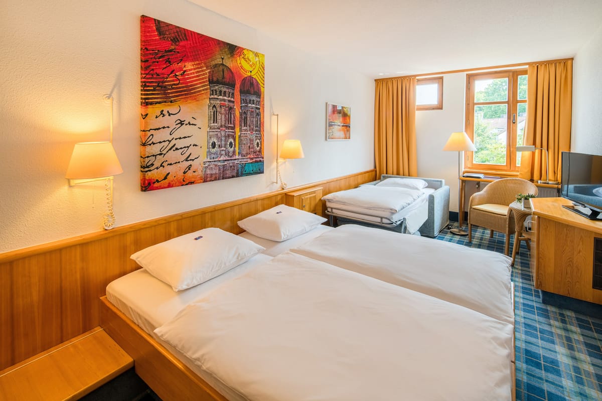A hotel room with two beds, a desk, a chair, a television, and artwork on the wall.