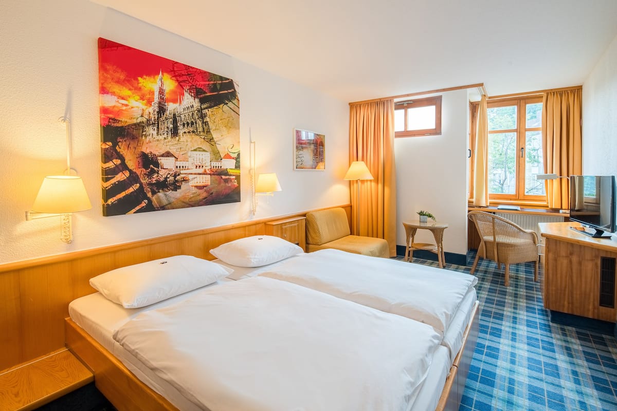 A hotel room with a large bed, two bedside tables, a desk with a chair, a TV, and a painting on the wall.