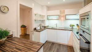 Una cocina moderna con armarios blancos, encimera de madera y horno empotrado.