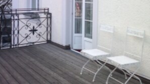A building with a wooden deck and two white metal chairs. - Hotel Galleria (Munich)