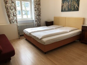 A bedroom with a bed, a radiator, a window with curtains, a painting on the wall, and a wooden floor. - Hotel Galleria (Munich)