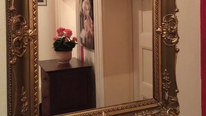 A mirror with an ornate gold frame, reflecting a door and a small table with a potted plant. - Hotel Galleria (Munich)